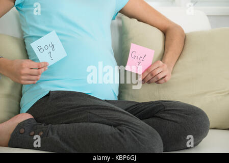 Midsection of pregnant woman holding notes with boy and girl written on it at home Stock Photo