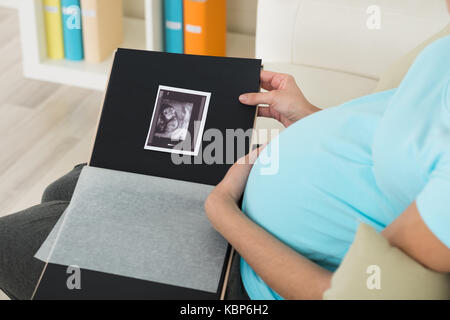 Midsection of pregnant woman with ultrasound scan sitting on sofa at home Stock Photo