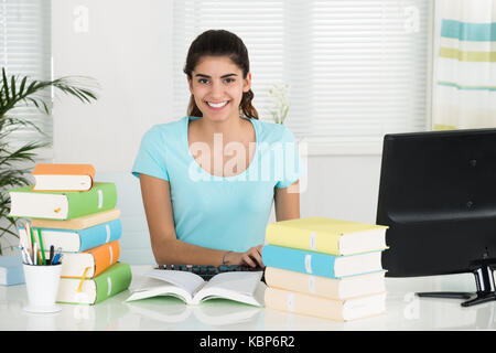 Portrait of happy female student using computer while studying at table in home office Stock Photo