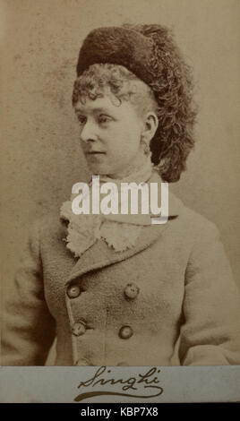 American archive monochrome studio portrait photograph of a young woman wearing an outdoor coat and feathered hat taken in late 19th century by Singhi photographers in Binghamton, NY, USA printed on embossed card mount with the photography studio name Stock Photo