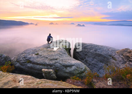 Sharp rear man silhouette on rocky peak. Satisfy hiker enjoy view. Tall man on rocky cliff watching down to landscape. Vivid and strong vignetting eff Stock Photo