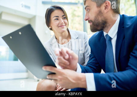 Group of hard-working colleagues brainstorming on joint project while gathered together at spacious meeting room Stock Photo