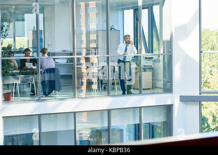 Interior of busy open plan office: creative designers brainstorming on joint project, middle-aged entrepreneur conducting telephone negotiations with  Stock Photo