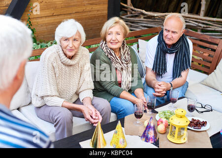 Senior friends wearing warm clothes having good time together while gathered together at lovely outdoor cafe, they listening to unrecognizable elderly Stock Photo