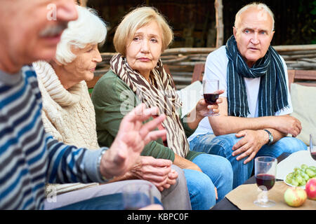 Long-awaited gathering of childhood friends: senior women and men wearing warm clothes sitting at outdoor cafe table and remembering pleasant moments  Stock Photo