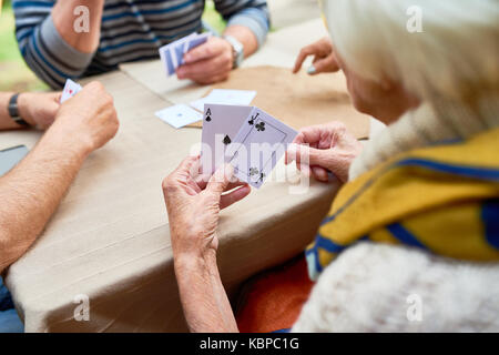 Close-up shot of unrecognizable senior woman playing poker with friends while sitting at outdoor cafe table, over shoulder view Stock Photo