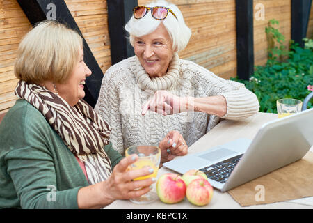 Smiling senior friends having fun together: they breathing fresh air outdoors and watching their favorite TV series on laptop Stock Photo