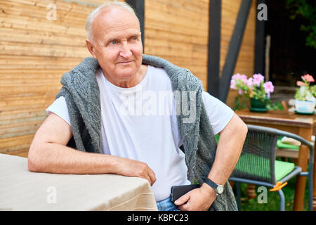 Portrait of handsome senior man with deep blue eyes looking away thoughtfully while sitting at outdoor cafe table and waiting for his order Stock Photo