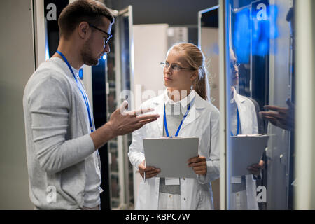 Portrait of  two scientists, man and woman, standing by server cabinets and discussing data while working with supercomputer in research center Stock Photo