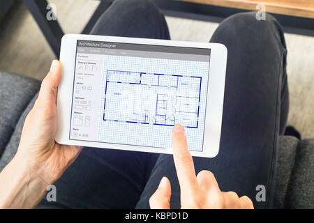 Person sketching a home design architecture project on a digital tablet computer app showing a blueprint floor plan drawing Stock Photo