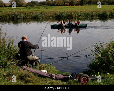 Old man fishing on the River Avon with kayakers paddling past, Tewkesbury, Gloucestershire, UK Stock Photo