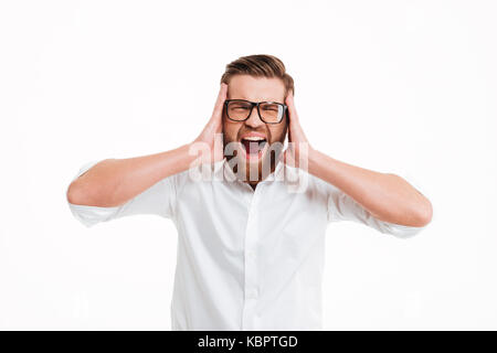 Image of screaming angry young bearded man standing over white wall background isolated. Eyes closed. Stock Photo