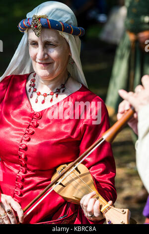 England, Sandwich. Living history re-enactment. Elderly Medieval costumed woman in red dress playing a rebec, the fore-runner to the violin. Stock Photo