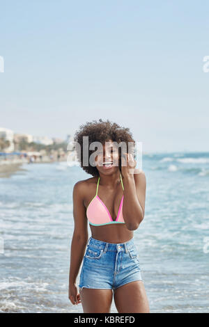 Portrait of pretty afro american girl standing in sea holding hand on hair laughing Stock Photo