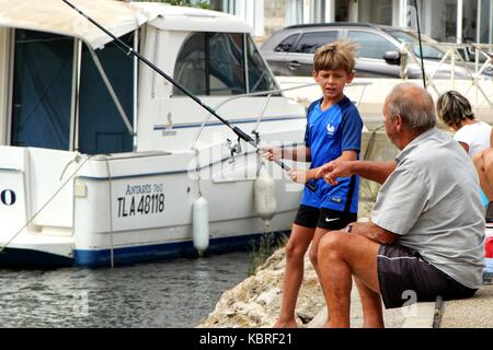 Older man teaching a young boy how to fish in a small harbour Stock Photo