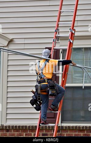 Solar panel technician carrying solar panels up ladder onto the roof of a house Stock Photo