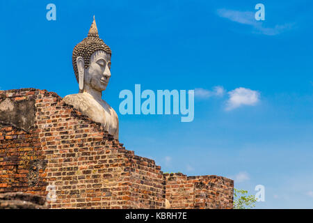 old buddha statue standing tall behind ruined temple wall and deep blue sky background in Ayudhaya, Thailand Stock Photo