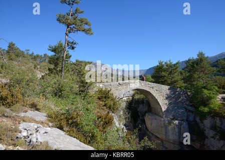 Walker Crossing Humpback Bridge, the Pont de Sautet (1787), over Jabron River, near Trigance, in the Verdon Gorge Regional Park Provence France