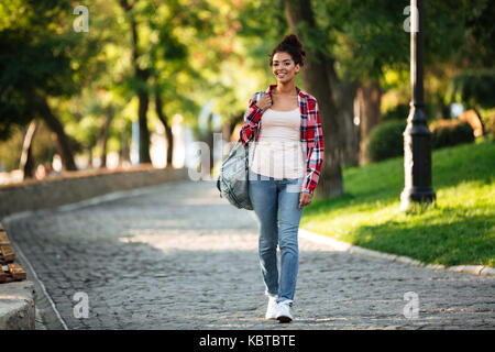 Picture of smiling young african woman walking outdoors in park. Looking aside. Stock Photo