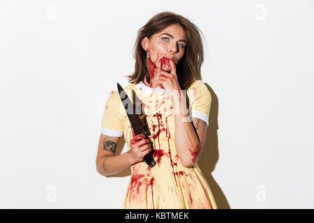 Creepy zombie woman covered in blood stains holding a knife and looking at camera isolated over white background Stock Photo