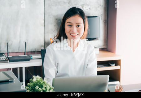 Asian businesswoman working with laptop computer on desk with smiling face,Happy office life concept,working woman at modern home office Stock Photo