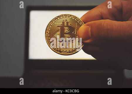 Bitcoin gold coin in the hand of man on the background of the laptop. Electronic money mining concept Stock Photo