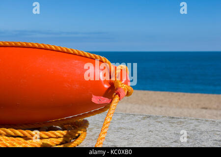 Close-up of bright orange buoy or fender with nylon rope against a deserted beach background at Slapton Sands, Devon, UK Seafood Coast Stock Photo