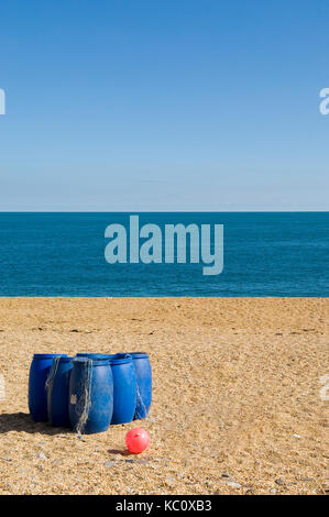 Group of blue plastic barrels on the beach at Slapton Sands, Torcross, Devon with the sea and a clear blue horizon in the background. Seafood Coast Stock Photo