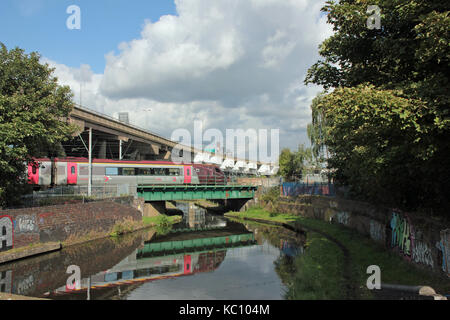 A Cross Country train is reflected in the water as it crosses a canal at Spon Lane near Smethwick under the M5 Oldbury viaduct in the Black Country. Stock Photo