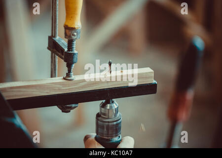 Man using the drill makes a hole in wood and iron strap. The process of making desk, furniture Stock Photo