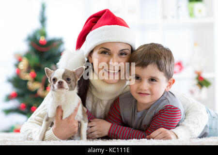 Woman and son celebrating christmas with furry friend. Mother and kid with terrier dog. Pretty child boy with puppy at x-mas tree. Stock Photo