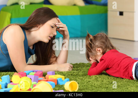 Angry baby and tired mother lying on a carpet in a room Stock Photo