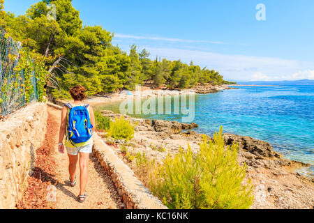 Young woman tourist with backpack walking on coastal path along sea near Bol town, Brac island, Croatia Stock Photo