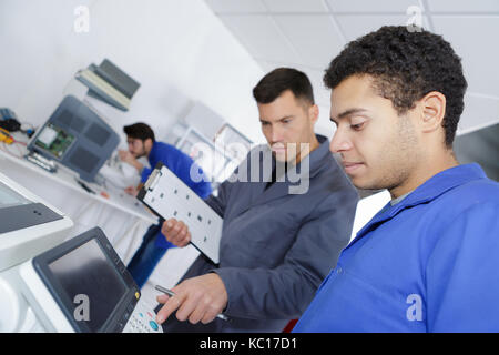 male apprentice working with engineer on cnc machinery Stock Photo