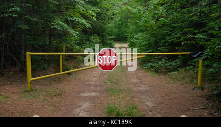 Yellow metal gate with red and white stop sign on a dirt road in the Adirondack Park forest. Stock Photo