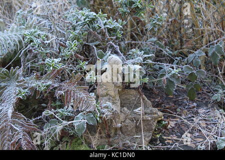 Old lady statue sit amongst frost covered plants Stock Photo