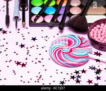 Holiday party makeup cosmetics. Color glitter eyeshadow, blush, liquid eyeliner, mascara, brushes with lollipop and confetti Stock Photo