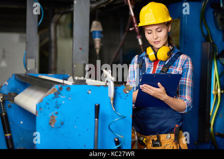Portrait of smiling young woman wearing  hardhat writing on clipboard  working in modern plant Stock Photo