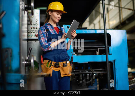 Portrait of female machine operator using digital tablet while working with power units in modern factory Stock Photo