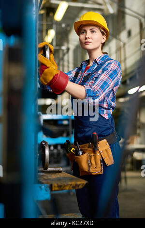 Portrait of female factory worker setting up machine units looking away  in modern plant Stock Photo