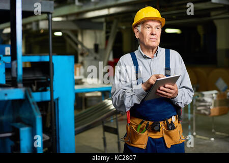 Portrait of senior factory worker using digital tablet looking away, copy space Stock Photo