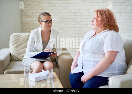 Portrait of obese young woman opening up to female psychiatrist during therapy session  on mental issues Stock Photo