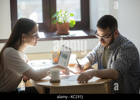 Two businesspeople seal a deal. Businessman reads paperwork carefully before signing. Female broker showing to the new owner  of a house where he has  Stock Photo