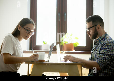 Man and woman working on laptops in a cafe, making notes. Remote working, freelance concept. Stock Photo