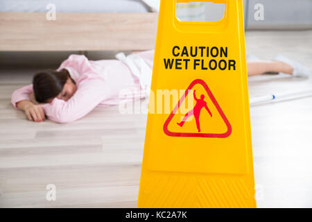 Close-up Of A Wet Floor Sign With Fainted Housekeeper Lying On Floor Stock Photo