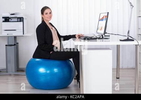 Pregnant Businesswoman Sitting On Fitness Ball While Working On Computer In Office