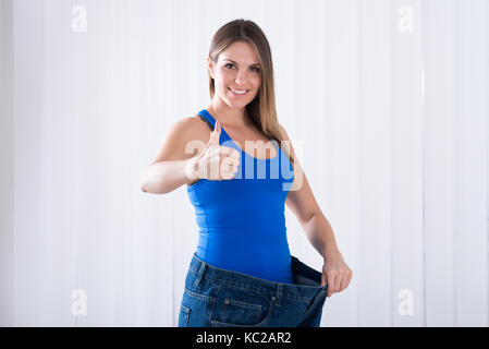 Happy Young Woman Showing Her Weightloss By Wearing Old Jeans Stock Photo