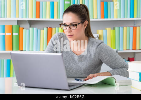 Young Woman Sitting In Library Using Laptop Stock Photo