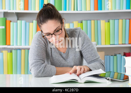 Photo Of Young Woman Reading Book In Library Stock Photo