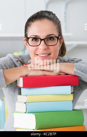 Happy Woman Leaning On Stack Of Multicolored Books At Desk Stock Photo